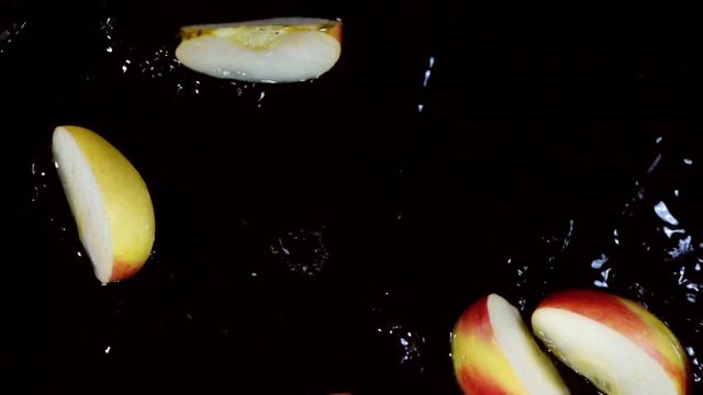 Juicy apple falling into wedges on wet black background and splashing in slow motion. Shooting with high speed camera. Overhead top view.
