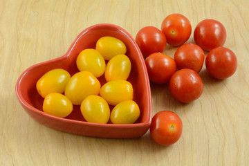 Red and yellow cherry tomatoes in and outside of red heart shaped bowl 