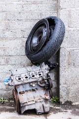 Old engine and car wheel with tyre dumped against an old breeze block wall.