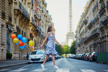 Beautiful young girl with colorful balloons running across the street in Paris