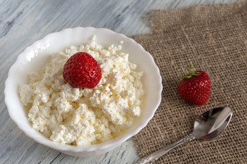 Grainy curd with strawberries on the table with canvas tablecloth.