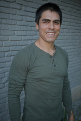 Obraz premium Handsome Smiling Ethnic Man in Front of Brick Wall