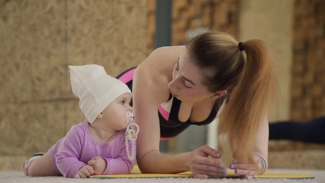 Mother and baby are engaged in fitness pose strap on the mat.