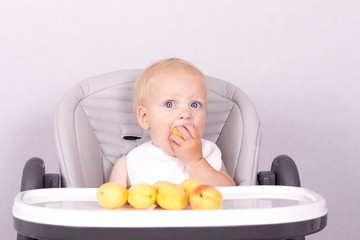 Funny toddler eating an apricot in baby chair against the grey background