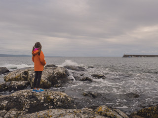 Young girl in orange coat watching waves, West Coast of Ireland.