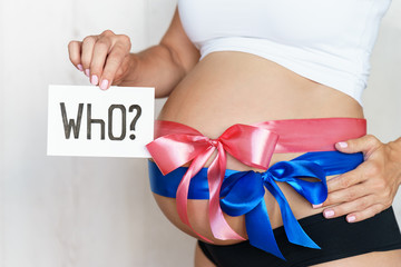 tummy with blue and pink ribbon bow of pregnant caucasian woman which is holding question who