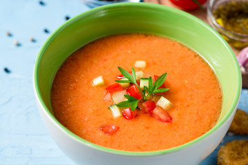 Summer cold soup gazpacho with parsley and vegetables on blue concrete background.