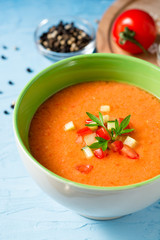 Summer cold soup gazpacho with parsley and vegetables on blue concrete background.