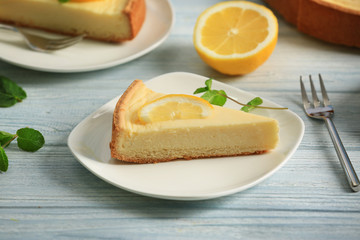 Plate with delicious cheesecake and slice of lemon on wooden table