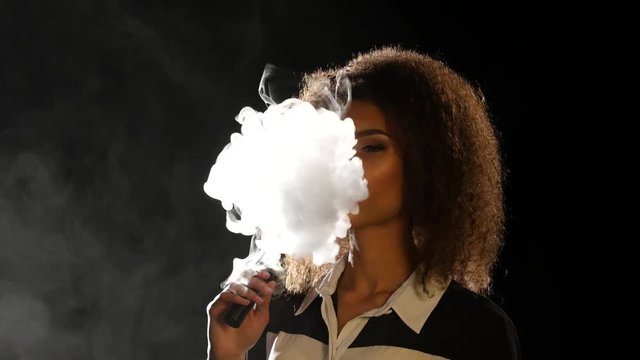 Beautiful woman smoking an e-cigarette Black background