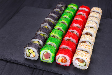 Delicious fresh multicolored sushi set on black slate, close-up. Traditional japanese food, restaurant serving