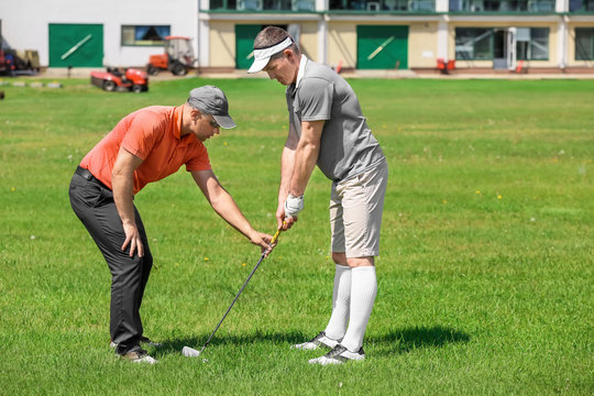 Caddy Teaching Young Man To Play Golf On Course In Sunny Day