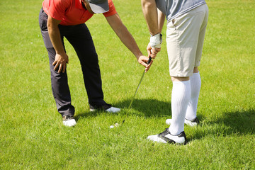 Caddy teaching young man to play golf on course in sunny day