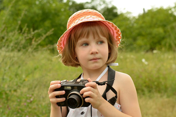 portrait of a baby photographer (a little girl) with a camera on the background of nature