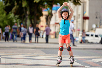 Funny Little pretty girl on roller skates in helmet riding in a park.