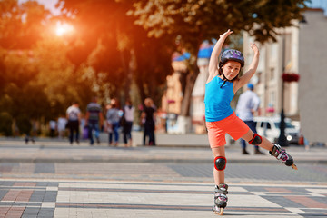 Funny Little pretty girl on roller skates in helmet riding in a park.