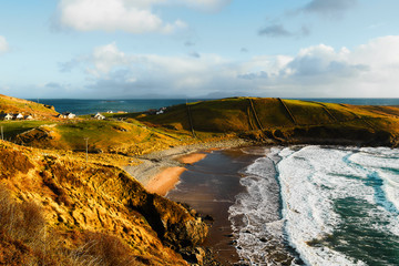 Wonderful coastline of Donegal ireland during the sunset in the summer with big waves, a blue sky and a small village with houses in the background