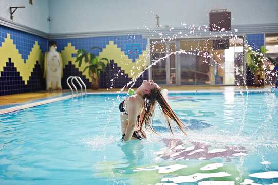 Portrait of a gorgeous firl in bikini making a splash with her hair in the pool in water park.