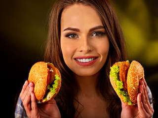 Woman eating hamburger. Student consume fast food. Girl holding two small burger . Girl trying to...