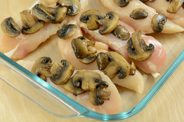 Making casserole sauteed mushroom slices on raw chicken beast tenderloins in glass baking dish