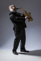 Naklejka premium Music Concepts. Full Length Portrait of Mature Expressive Caucasian Saxophone Player in Sunglasses Playing the Saxophone in Studio Environment.