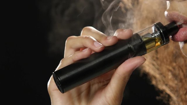 Lips of a girl of african american appearance smokes an vaping. Black background. Close up