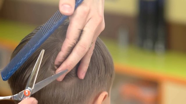 Barber cuts the hair of boy with scissors in the salon