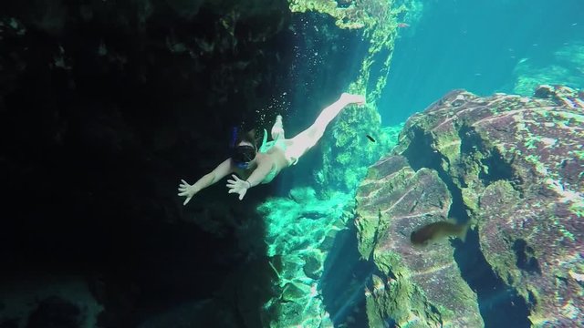 UNDERWATER, SLOW MOTION: Young woman in bikini freediving in gorgeous crystal clear lake exploring beautiful rocky river bottom in Gran Cenote cave, Mexico, Yucatan. Girl on summer vacation swimming
