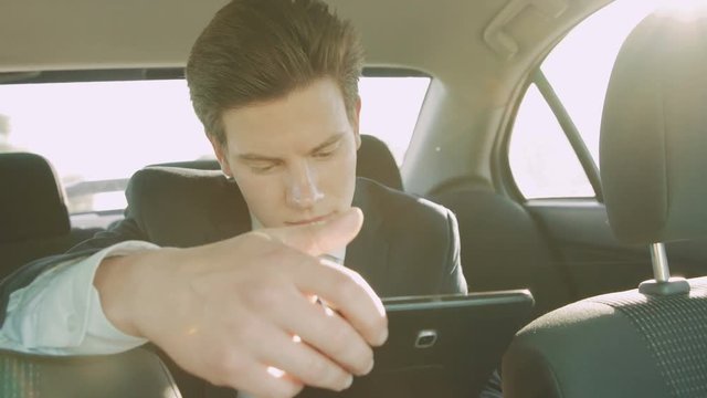 Smiling young businessman hurries up in the car and using tablet 4K