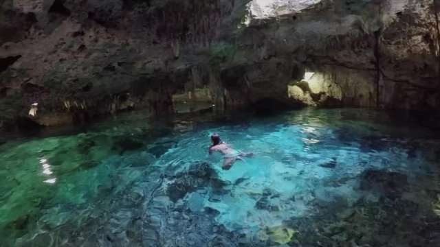 CLOSE UP Young woman swimming in turquoise pool in breathtaking underground cave. Tourists exploring a fascinating architecture of the stalactites and stalagmites in Aktun Chen cenote sinkhole, Mexico