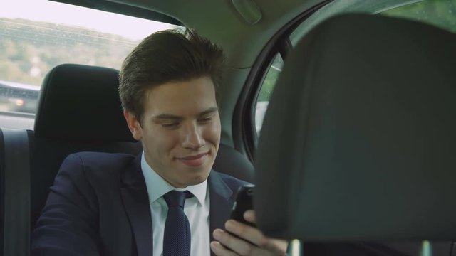 Young businessman going in the car and using the smartphone 4K