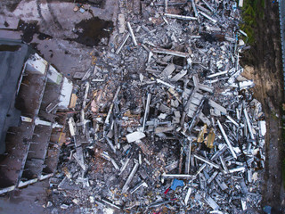 A process of buliding demolition, demolition site with heavy bulldozer and excavator with crushing equipment at work, demolished house, shot from air with drone
