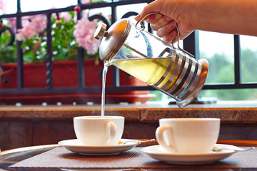 A woman pours tea from a teapot into a cup.