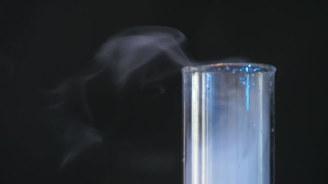 glass flask with chemicals and dry ice on a dark background. Chemical reaction of blue liquid in raduated cylinder in labolatory