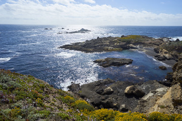waves are crashing against coastal rock formations at California's pacific coast with the afternoon marine layer forming and bringing mist towards land