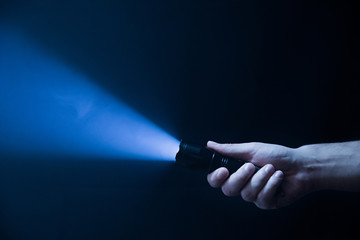 The flashlight in the man's hand from the right side of the frame in black and blue color isolated on black background - obrazy, fototapety, plakaty