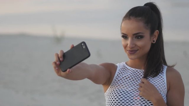 Beautiful brunette doing selfie on the beach. Young woman in summer on the beach taking pictures of herself on a smartphone.
