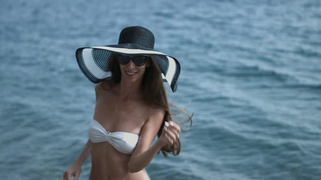 Tall slender girl in the hat and sunglasses posing while standing in the bikini