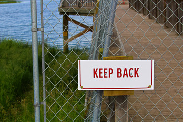 A keep back sign on a chain-link fence