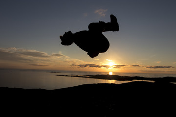 Silhouette parkour man jumping high on the mountain doing a backflip in the sunset