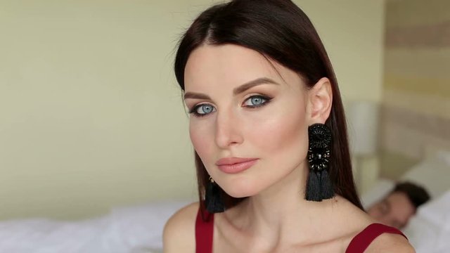 Portrait of a young beautiful girl in a bedroom near bed, in the background a blurred man. Portrait of a sad woman in bed with her husband.