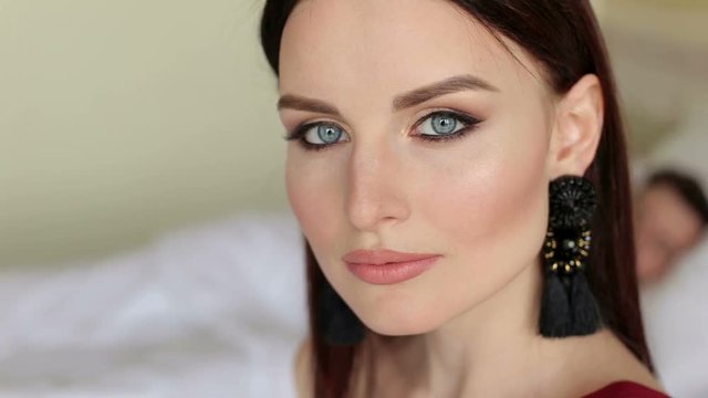 Close-up face of beautiful woman with blue eyes in bed hotel room, the background is blurred the man lying in bed.