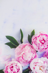 Minimal styled flatlay with peony flowers, petals and leaves on a pastel background with copy space