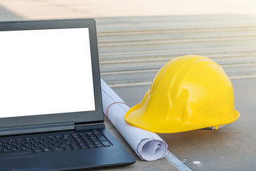 The safety helmet and the blueprint with laptop has white screen isolated at construction site