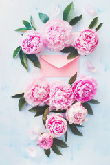 Minimal styled flat ay with peony flowers, petals and pink love letter envelope on a pastel background