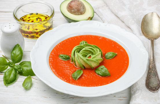 Delicious tomato soup with avocado, fresh Basil, olive oil and spices in a white plate on the table. The Mediterranean cuisine. Selective focus