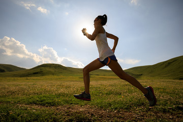 young fitness woman runner running on sunset grassland trail