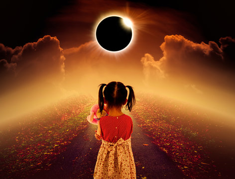 Total solar eclipse glowing above child on pathway with night sky and clouds