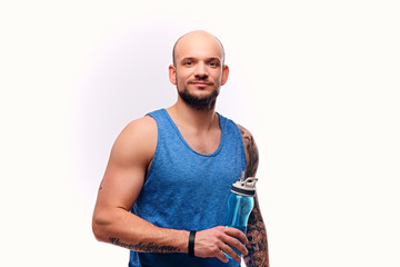 Shaved head sporty male drinks water.