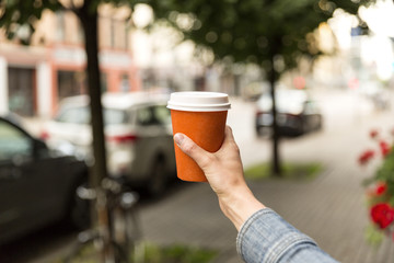 Woman's hand with coffee in paper cup, city view background